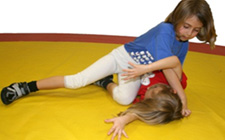 Due bambine lottano su un tappetino. Una è sdraiata sulla schiena mentre l'altra la tiene a terra da sopra.