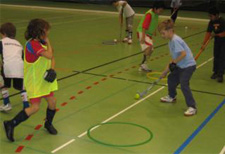 Dei bambini conducono una pallina con un bastone in una palestra.