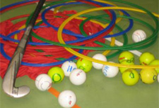 La foto illustra un bastone, delle palle, dei cerchi e dei nastri sul pavimento di una palestra.