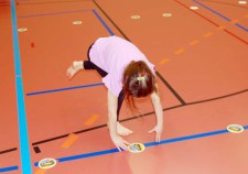 Una bambina chinata per sollevare un sottobicchiere dal pavimento di una palestra 