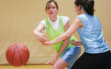 Junge Frau passt einen Basketball um eine Gegnerin herum einem Mitspieler.