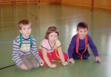 Drei Kinder knien nebeneinander am Boden und klopfen mit Flaschendeckel auf den Boden.
