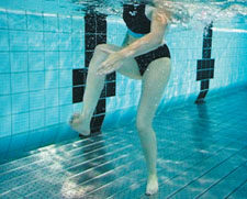 Una donna è in piedi in acqua poco profonda e tocca il piede destro con la mano sinistra.