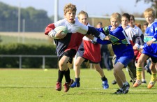 Diversi bambini ne inseguono un altro che porta la palla durante una partita di rugby.