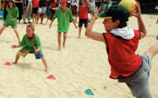 Kinder spielen auf Sand Tchoukball, ein Kind wirft gerade ab.