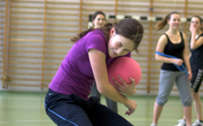 Junge Frau mit Ball in der Hand versucht, sich vor einem heranfliegenden Ball zu schützen.