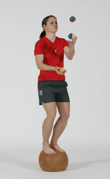 Une athlète est debout sur un ballon lourd et jongle avec trois balles.