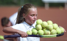 Ein Mädchen transportiert viele Tennisbälle auf einem Schläger.