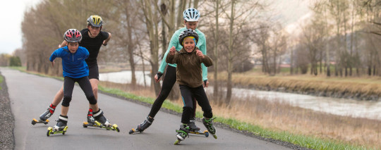 Trois garçons et une fille s'entraînent sur des rollers inline ou des skis à roulettes.