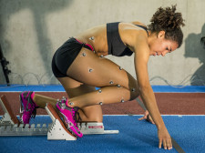 Une athlète est en position de départ dans les starting-blocks. Elle porte des capteurs sur le corps.