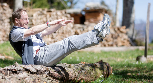 Un homme est assis sur un tronc d'arbre et tend les jambes et les bras vers l'avant.
