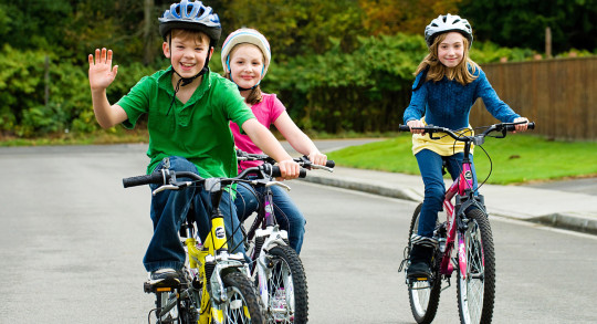 Trois enfants roulent à vélo sur une route de quartier.