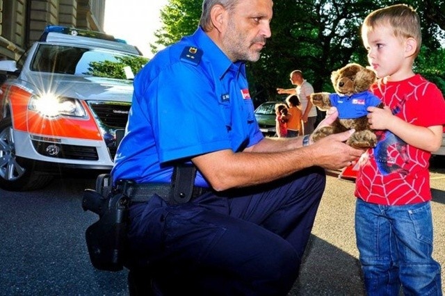 Polizist überreicht einem Buben einen Plüsch-Polizeibären
