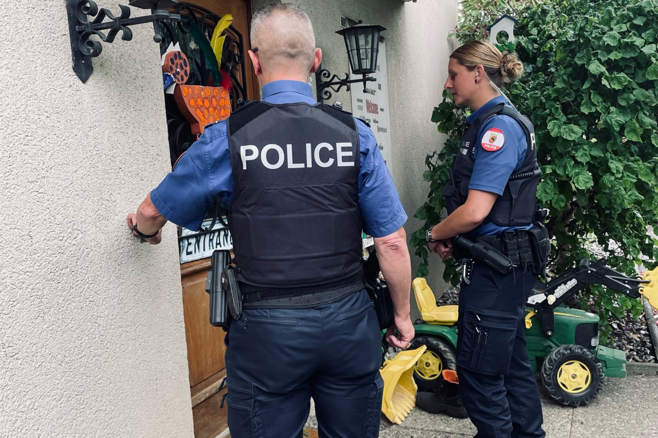 Eine Polizistin und ein Polizist stehen vor einer Haustür, der Polizist klingelt.