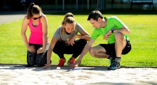 Athletinnen und Athlet im Sandkasten beim Anschauen eines Modells.