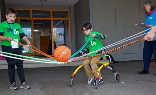 Zwei Kinder - eins im Rollstuhl - bei einem gemeinsamen Spiel. 