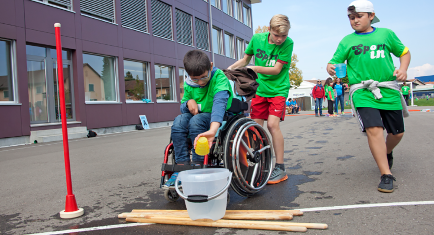 Trois enfants, dont un en fauteuil roulant verse le contenu de leur gobelet dans un seau.
