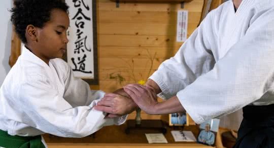 Un enfant réalise un exercice d'aïkido avec un enseignant.