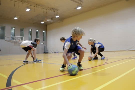 Des enfants jouent avec des balles dans une salle de sport.
