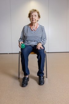 Una signora anziana seduta su una sedia si massaggia la coscia con una palla riccio