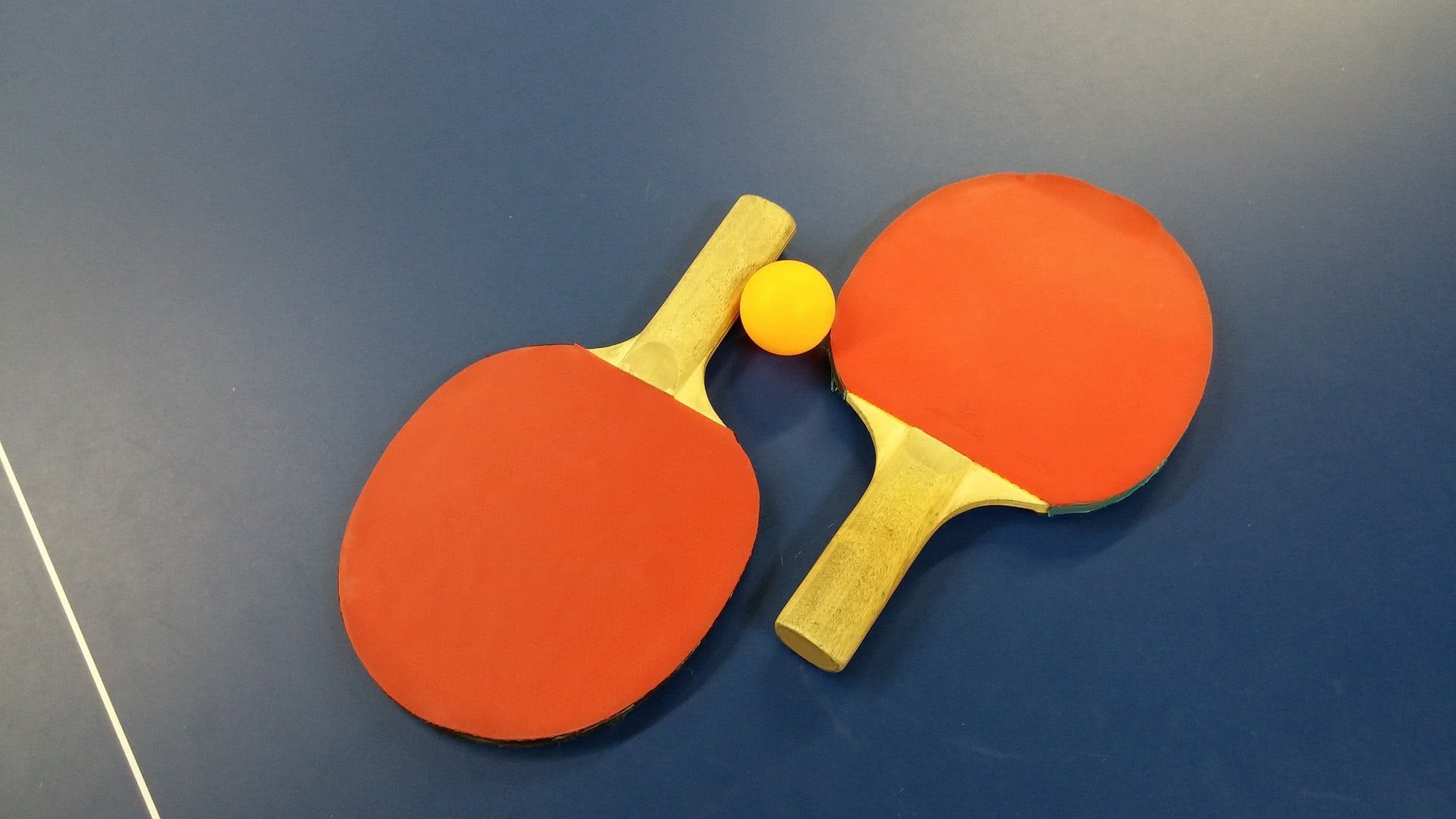 Due racchette da tennistavolo arancioni e una pallina gialla su un tavolo da ping pong blu