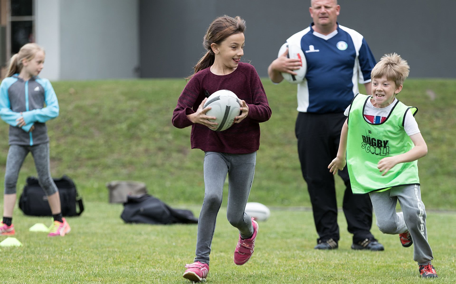 Photo: Poursuivie par un garçon, une jeune fille tient un ballon de rugby entre ses mains.