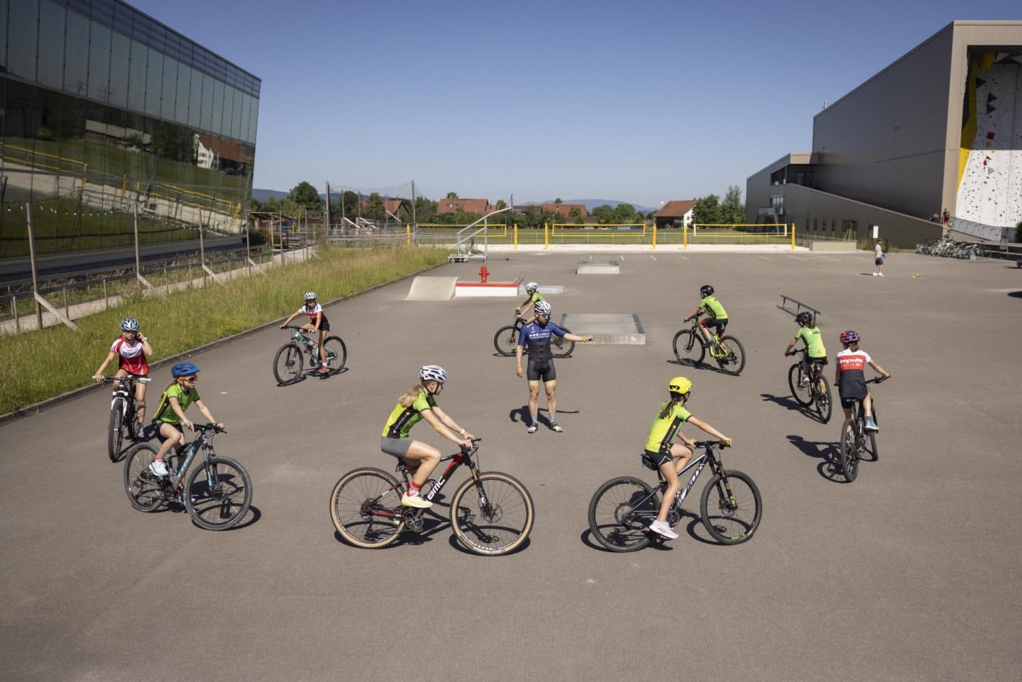 Des athlètes circulent à vélo en cercle sur une place de jeu bétonnée.
