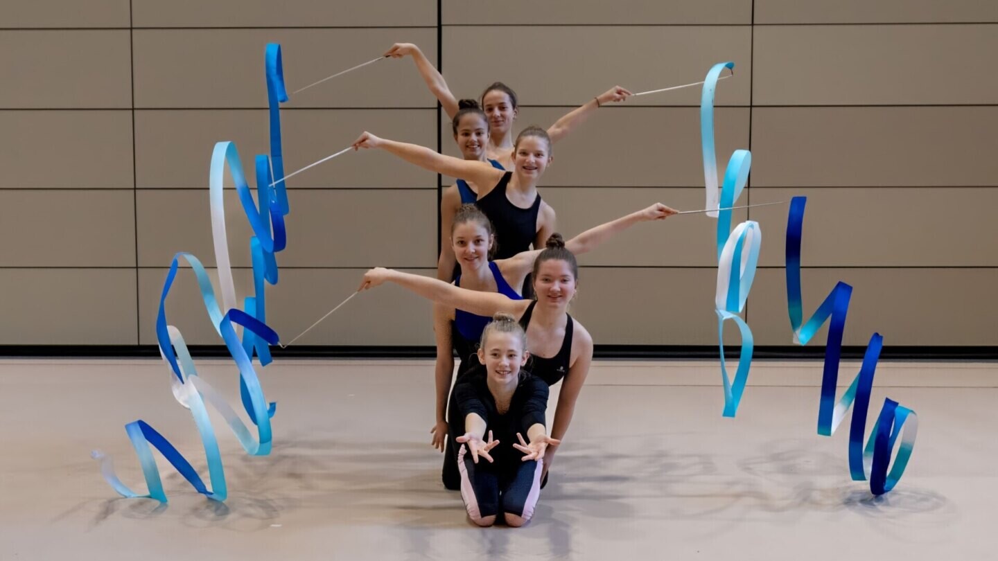 Gymnastinnen bilden eine Formation und schwenken blauweisse Bänder.