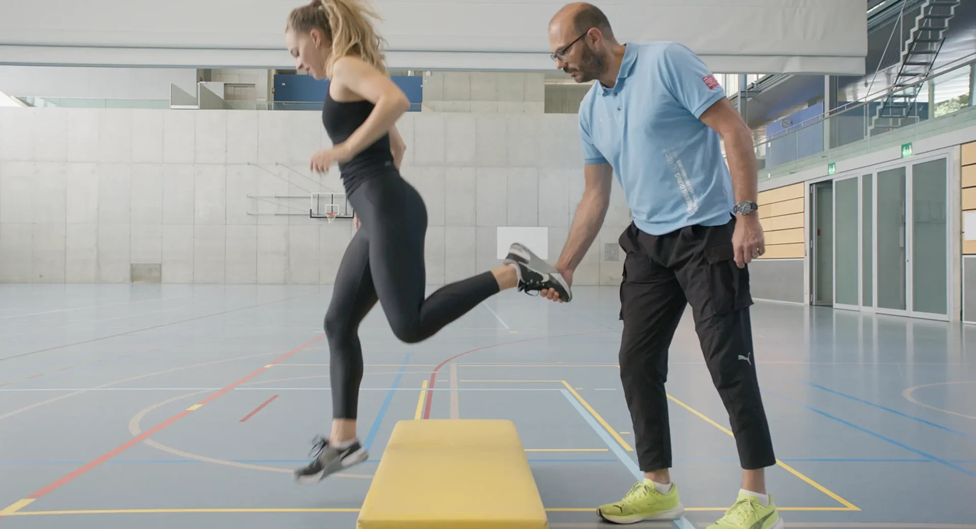 Trainer mit Athletin beim Einbeinsprung ab Schwedenkasten.
