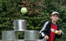 Foto: un bambino lancia una pallina da tennis contro delle scatole di latta