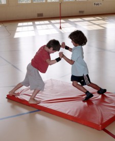 Due bambini in piedi su un tappetino si spingono con le mani intrecciate cercando di far cadere l'avversario dal tappetino