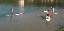 Drei Kinder in flachem Seewasser während sie auf ihren Kanu stehen (Stand Up Paddeling).