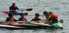 Kinder in offenem Wasser in Kanus in einer Viererreihe.
