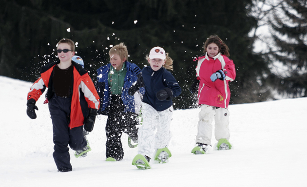 Quatre enfants courent dans la neige avec des raquettes.