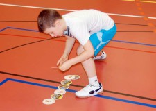 Un bambino dispone dei sottobicchieri su una linea sul pavimento di una palestra
