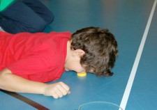 Un garçon est couché sur le ventre et touche une capsule de bouteille posée sur le sol avec son nez.