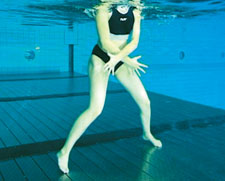 Une femme réalise l'exercice du pantin – mouvement inverse des bras et des jambes – en eau peu profonde.