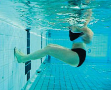 Unterwasseraufnahmen: eine Frau schwebt sitzend in brusstiefem Wasser und berührt mit den Füssen die Beckenwand. 