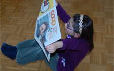 Ein Mädchen sitzt am Boden mit angewinkelten Beinen und liest eine Zeitung. 