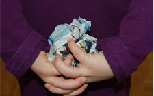 Un bambino tiene fra le mani, poste dietro la schiena, delle palle formate con pagine di giornale