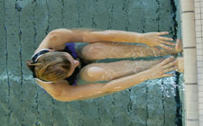 Una donna è in posizione dorsale, gambe raccolte e piedi appoggiati contro la parete della piscina.