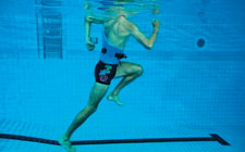 Un uomo esegue un esercizio in acqua poco profonda. Solleva la gamba sinistra accompagnando il movimento con le braccia.