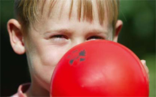 Primo piano su un bambino che gonfia un palloncino rosso.