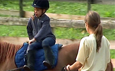 Un bambino sta scendendo da un pony seguito dall'occhio vigile di una monitrice.