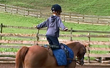 Un bambino è in ginocchio su un pony e allarga le braccia lateralmente per tenersi in equilibrio.