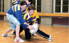 Zwei Kinder spielen Rugby, ein Kind hält das andere von hinten und versucht, ihm den Ball weg zu nehmen.