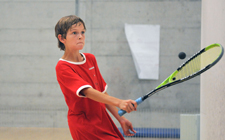 Un bambino lancia una pallina con una racchetta da squash.