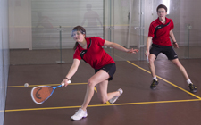 Una ragazza impegnata in una partita di squash contro un ragazzo.
