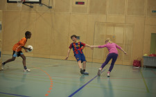 Ein Kind zieht das andere bei der Hand, ein anderes Kind rennt mit einem Ball auf beide zu.