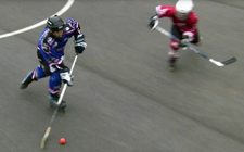 Un joueur de hockey inline conduit la balle tandis qu'un joueur de l'équipe adverse patine dans sa direction.